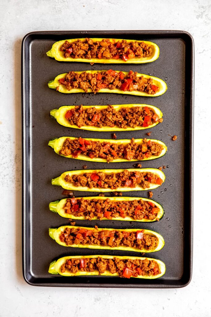 A sheet pan with the zucchini boats filled with taco meat.