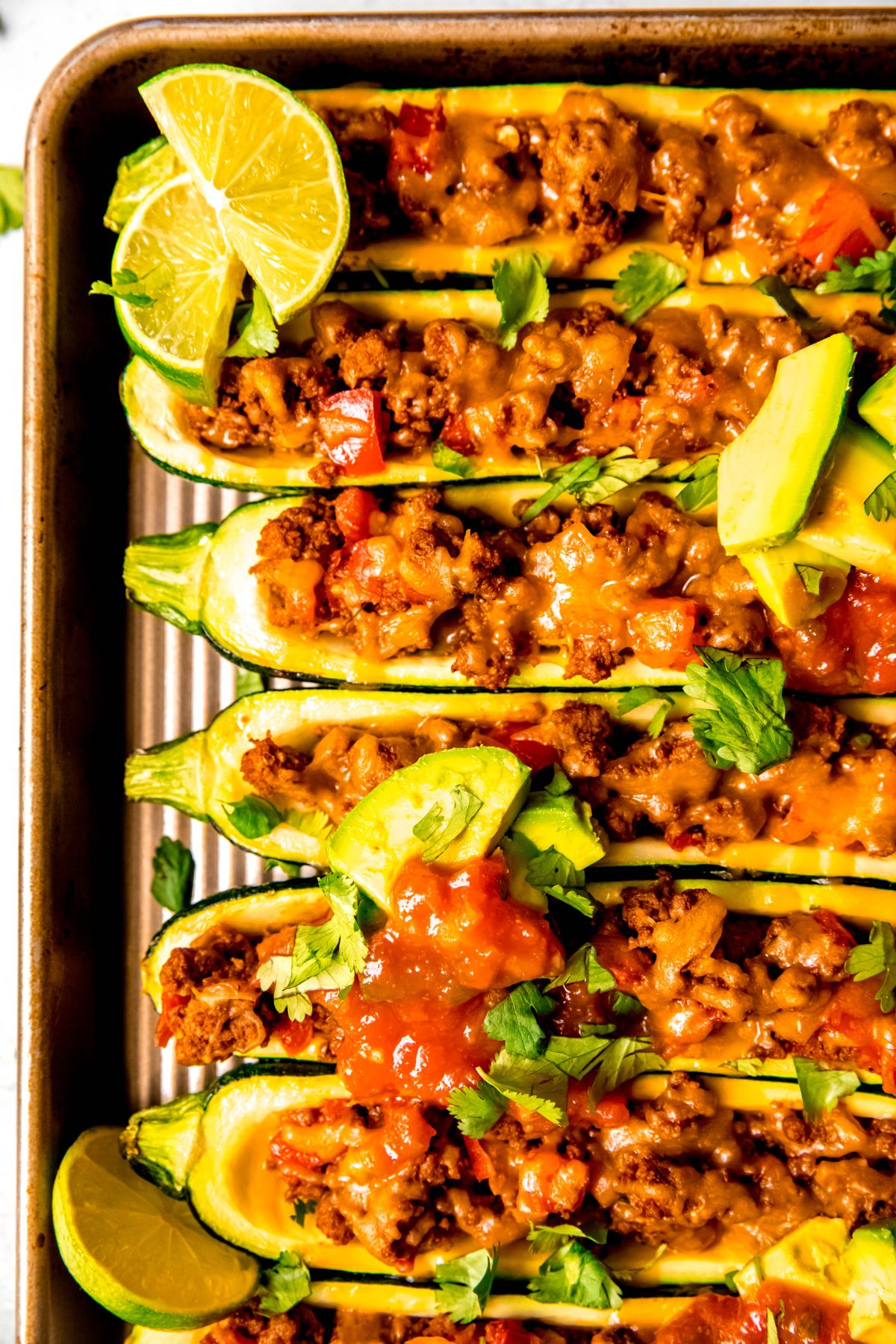 A close-up overhead shot of part of the taco zucchini boats with avocado, salsa, and cilantro.