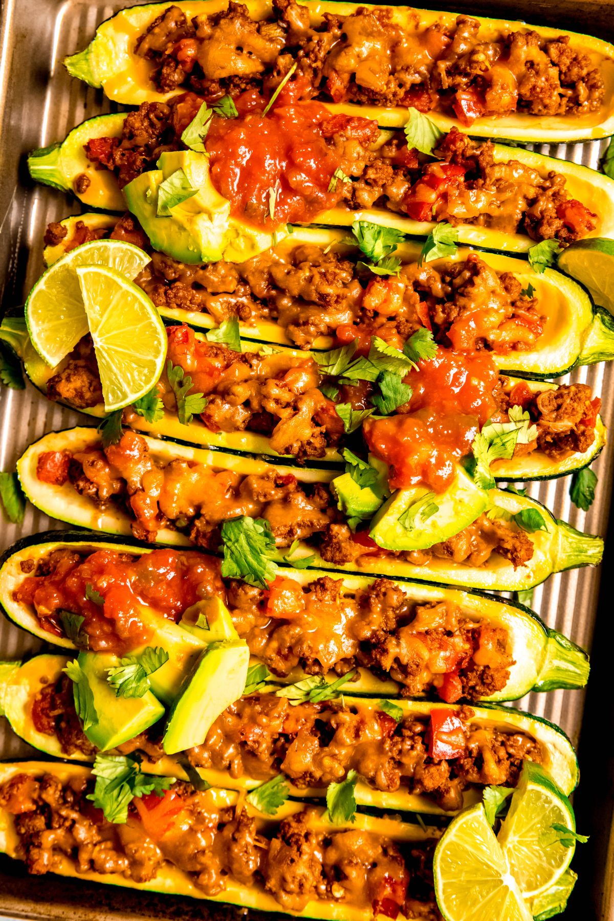 A close-up overhead shot of zucchini boats topped with avocado, cilantro, and salsa.