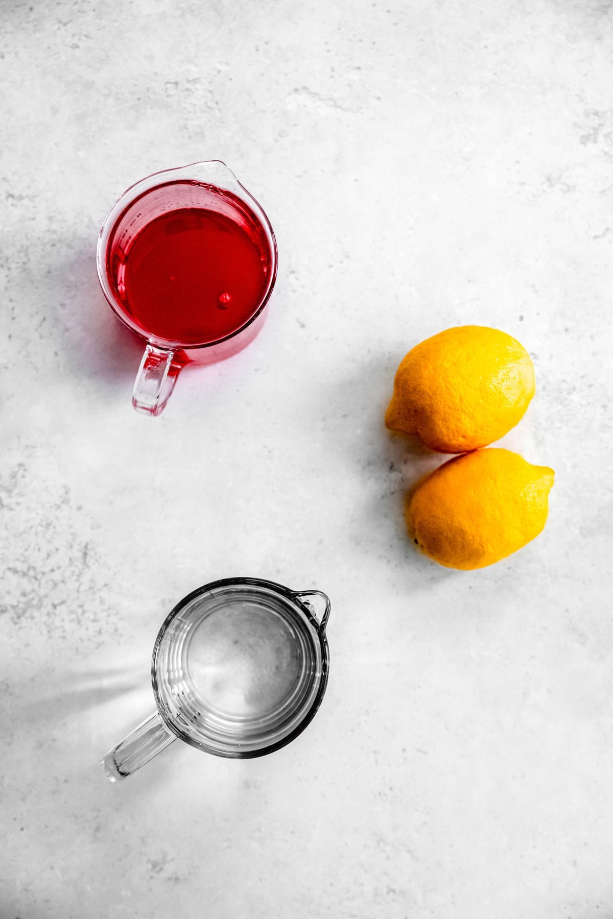 watermelon syrup, fresh lemons, and water measured out on a white table for making homemade watermelon lemonade recipe.
