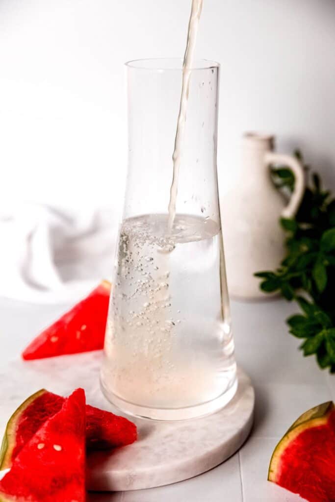 action shot of fresh lemon juice being added to a pitcher with water.