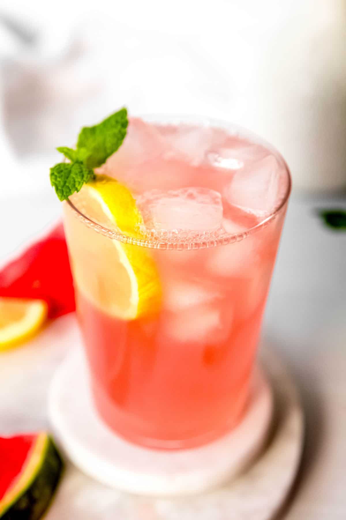 45 degree downward facing shot into a glass of pale pink watermelon lemonade garnished with fresh lemon and mint.