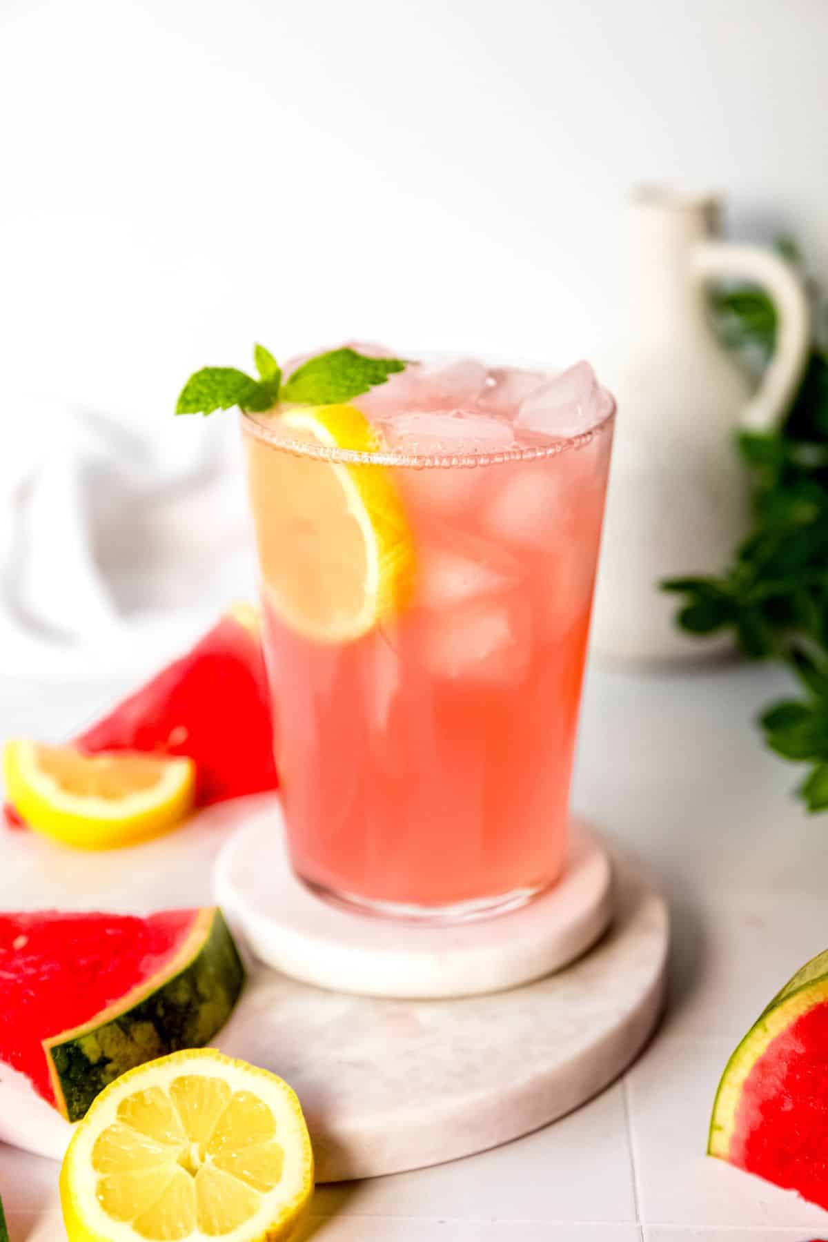 serving of watermelon lemonade on a table with fresh slices of watermelon and fresh lemons.