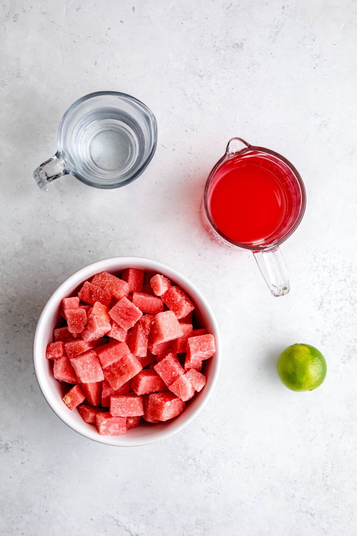 water, watermelon simple syrup, a fresh lime, and frozen watermelon chunks measured out for making homemade watermelon sorbet recipe.