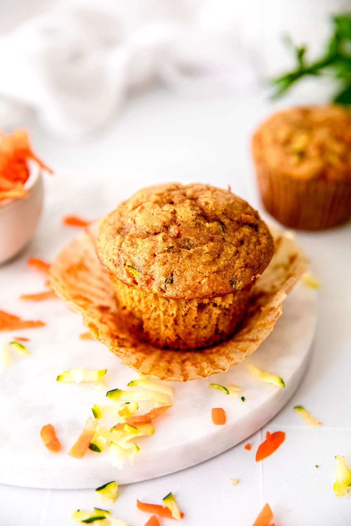 45 degree angle downward shot looking at the top of a healthy zucchini carrot muffin with the natural paper wrapper pulled away from the sides.