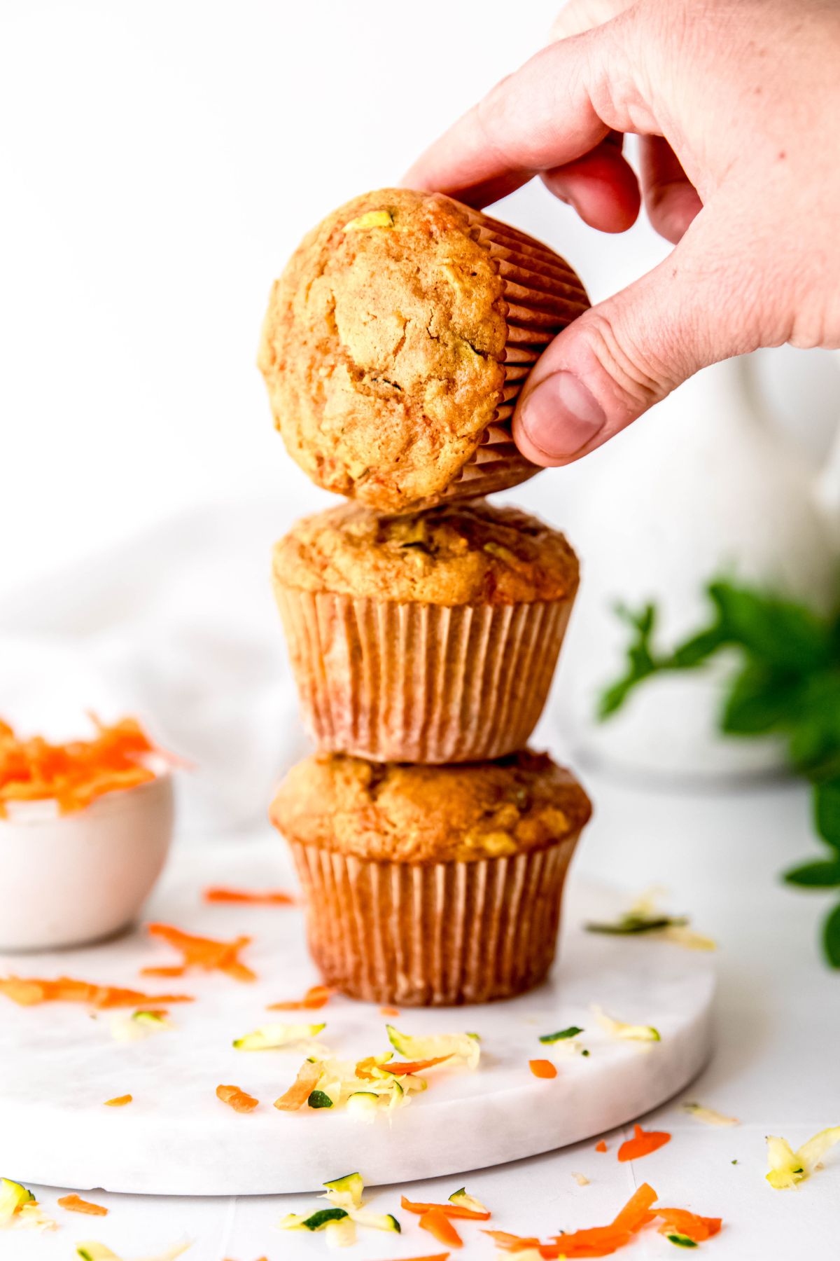 stack of three carrot zucchini bread muffins with a hand turning the top one on its side to show the crackly top.