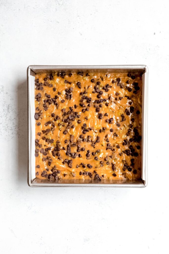 An 8x8-inch baking pan full of zucchini bar batter before baking.