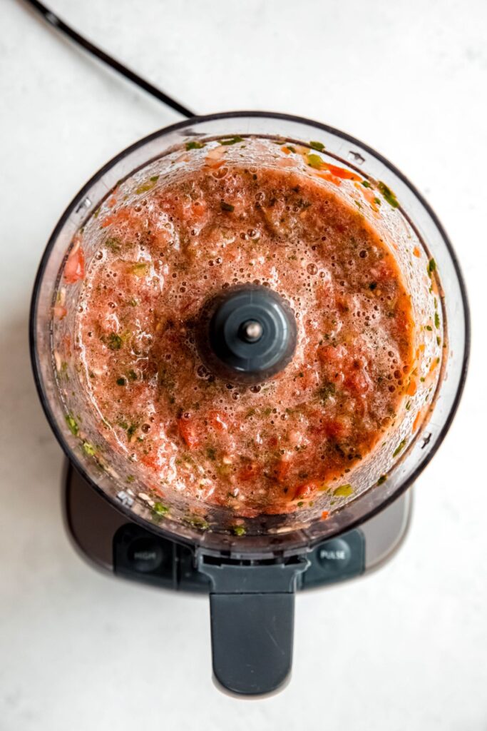 food processor bowl filled with slightly chunky restaurant style salsa with fresh tomatoes.