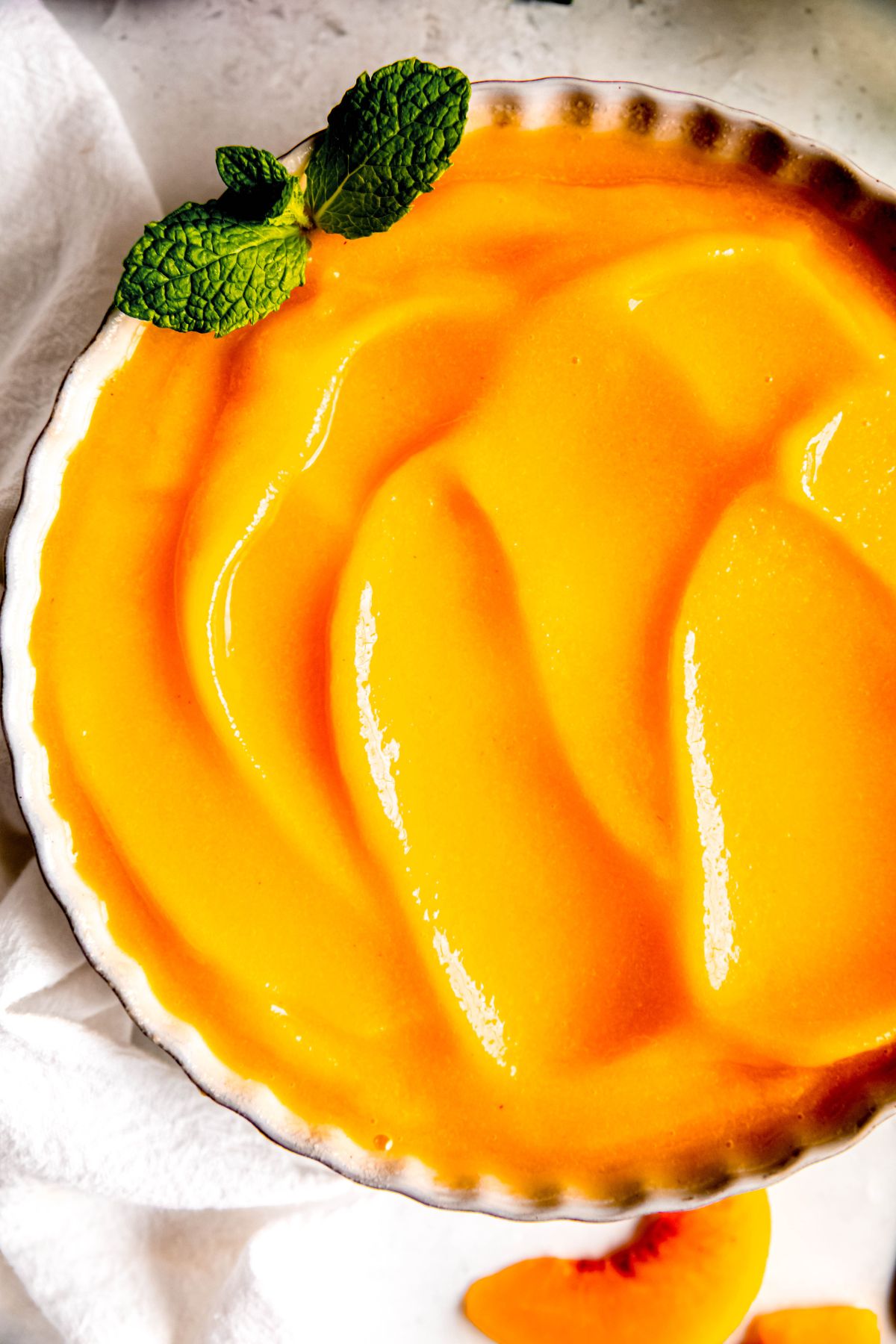 closeup shot of peach sorbet in a scalloped white bowl with divots created by smooshing it out with the back of a spoon.