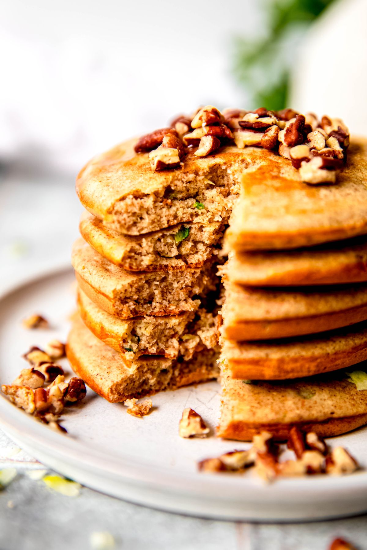 closeup shot of a stack of zucchini protein pancakes on a plate with a triangular shaped bite cut all the way through the stack revealing the fluffy interior.