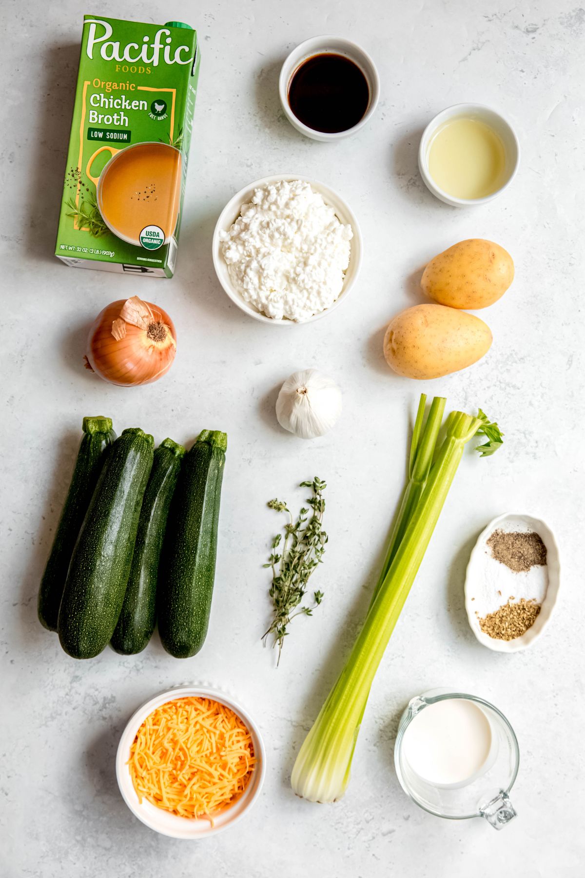 ingredients needed to make zucchini potato soup recipe measured out on a white table.