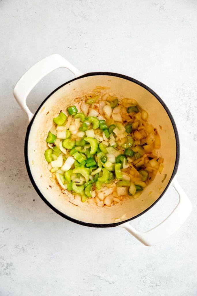 celery and onions being sautéed in a white dutch oven.