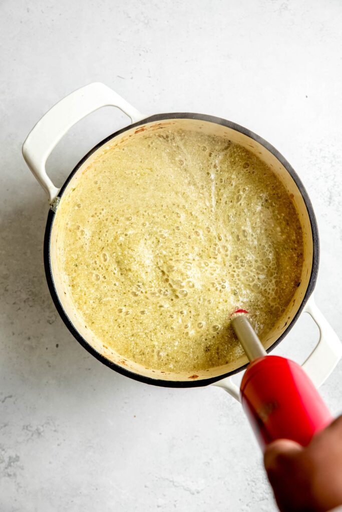action shot of a stick blender blending the potato zucchini soup until smooth and creamy.