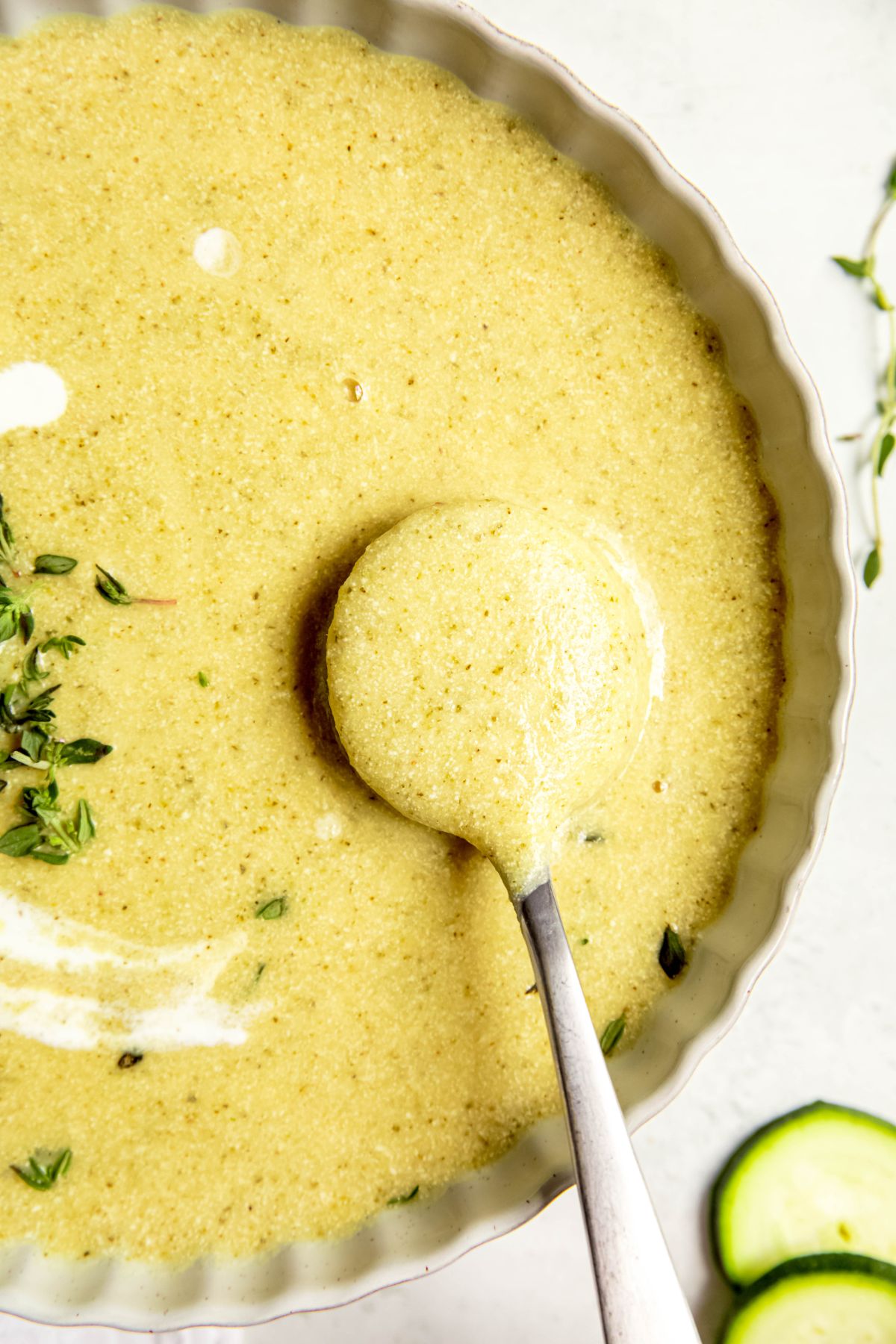 silver soup spoon with a spoonful of creamy potato zucchini soup slightly above the bowl.