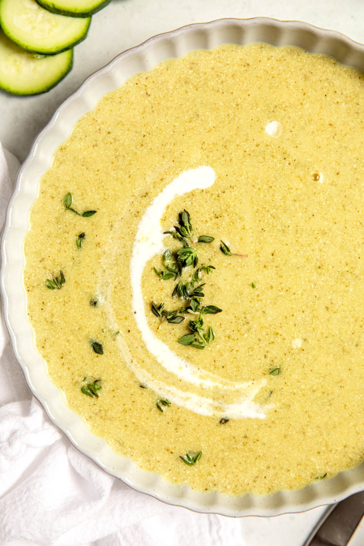 closeup overhead shot of the left side of a bowl of creamy zucchini potato soup garnished with fresh thyme leaves and a crescent moon shape drizzle of cream.