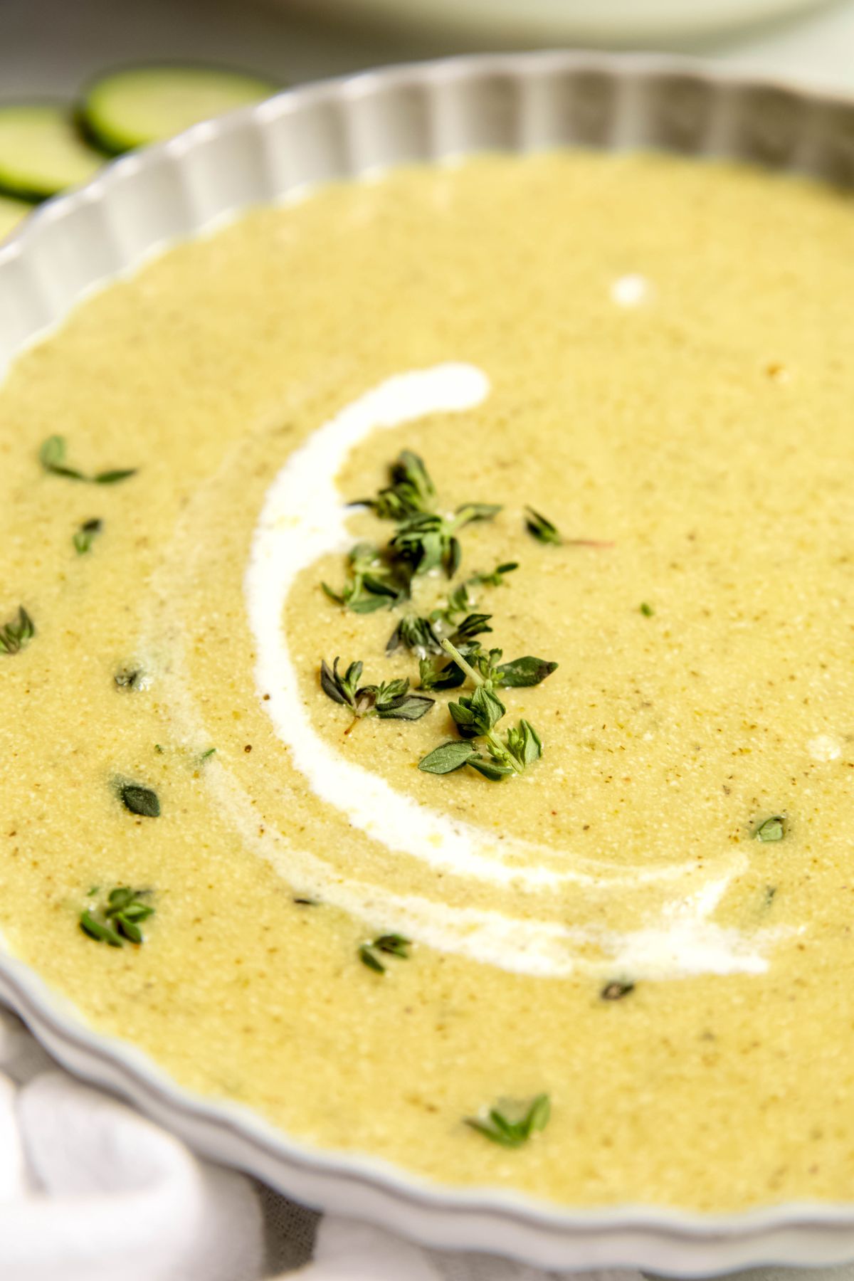 45 degree angle closeup shot of a bowl of blended creamy zucchini potato soup garnished with fresh thyme and a drizzle of cream.