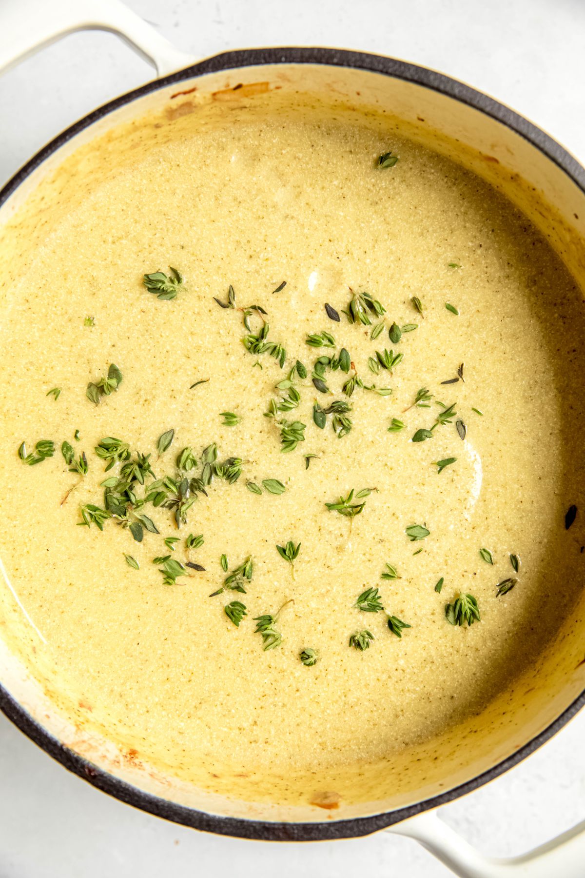 closeup shot of creamy potato zucchini soup in the dutch oven with a fresh sprinkle of thyme.