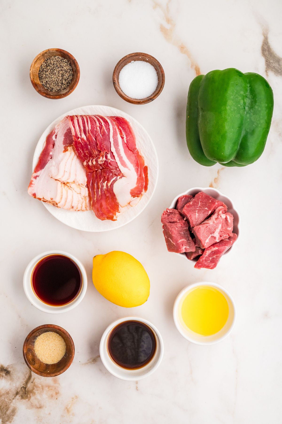 ingredients needed to make beef steak, bell pepper, and bacon skewers measured out on a white table.