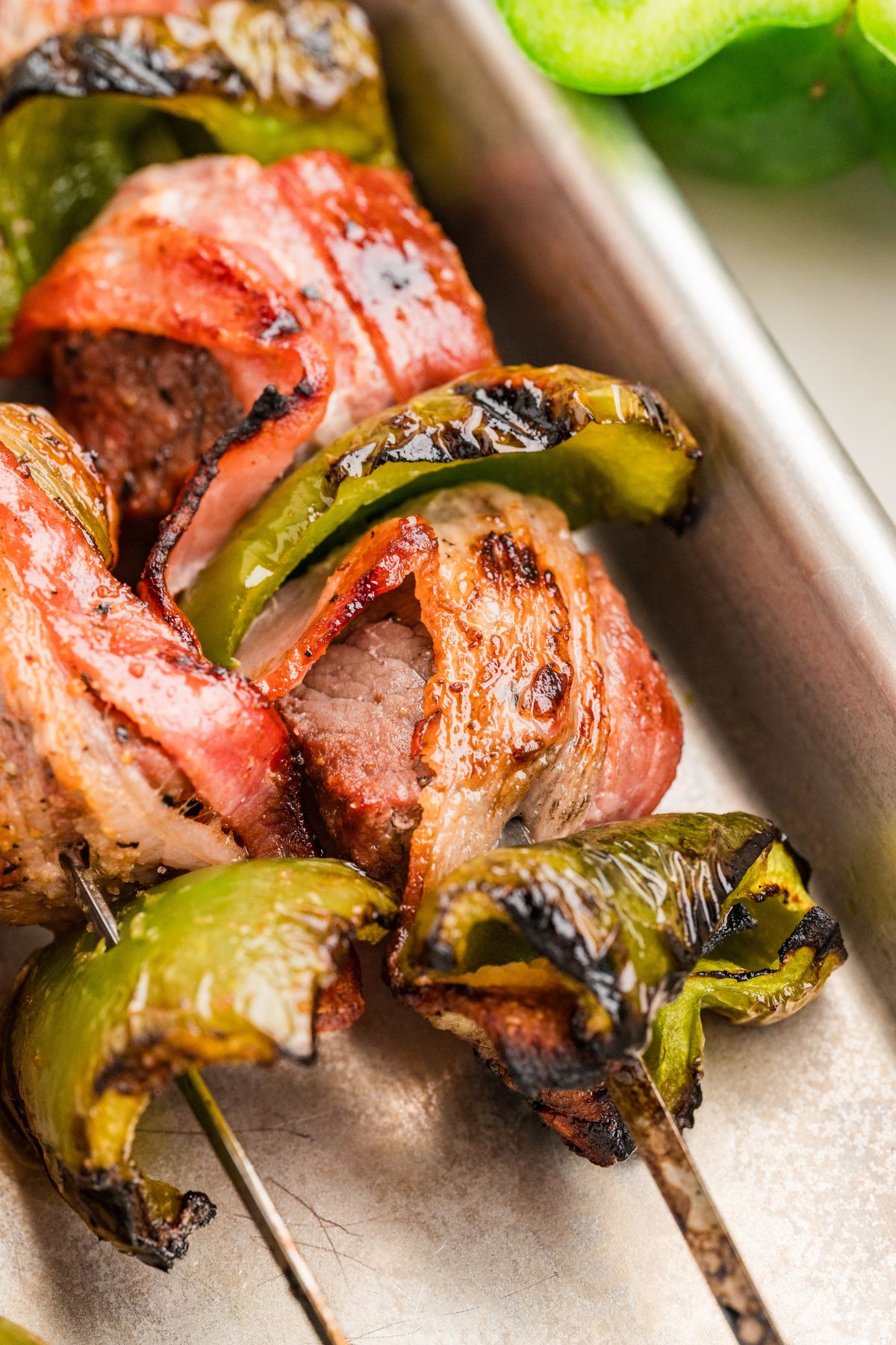 closeup shot of two bacon beef skewers on a rimmed baking sheet after grilling.