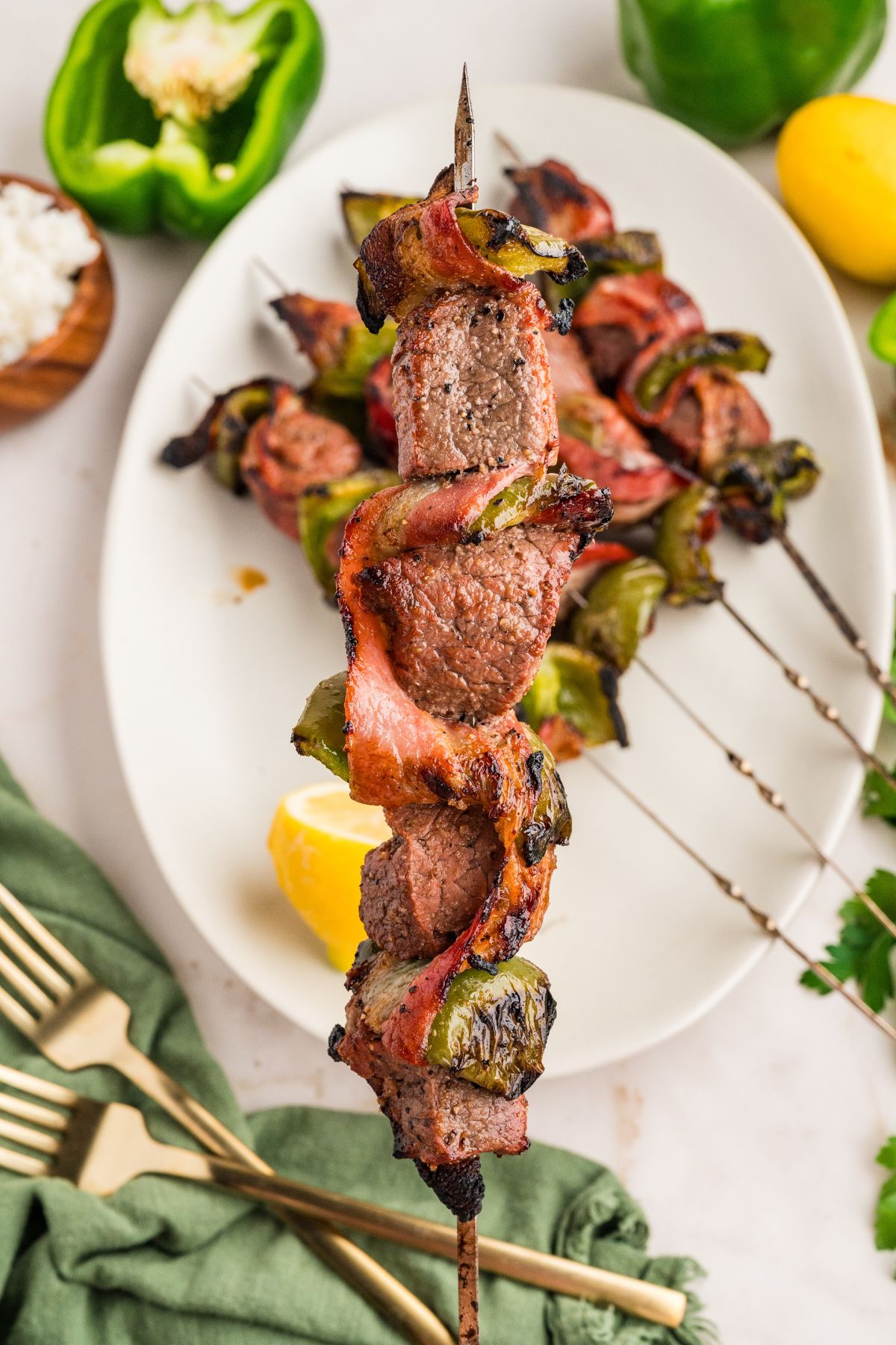 hand holding a single bacon beef steak skewer above the platter with the remaining skewers on it blurred out beneath.