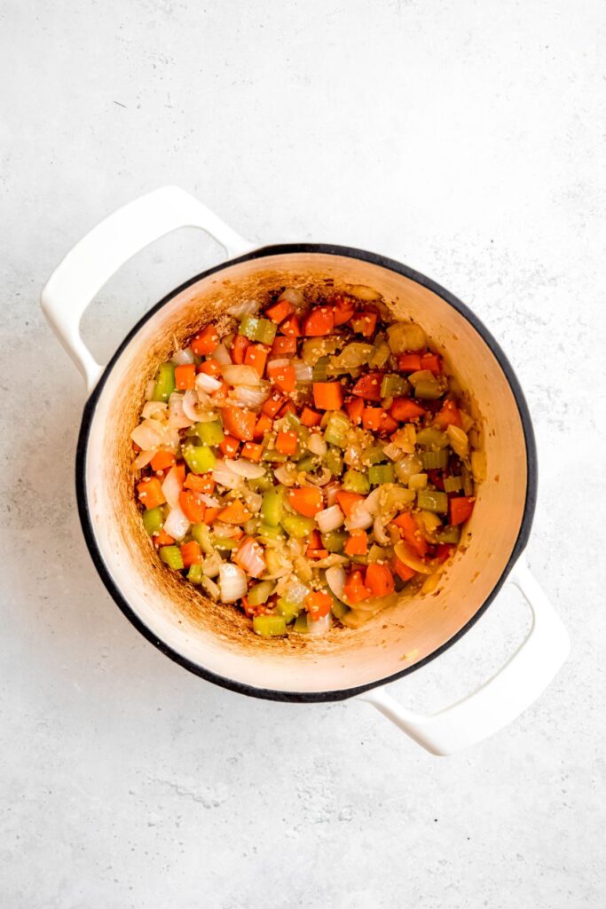 Sauteed veggies in a white Dutch oven pot.