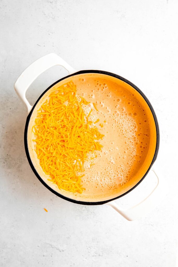 The creamy potato soup in a white pot with shredded cheddar cheese.