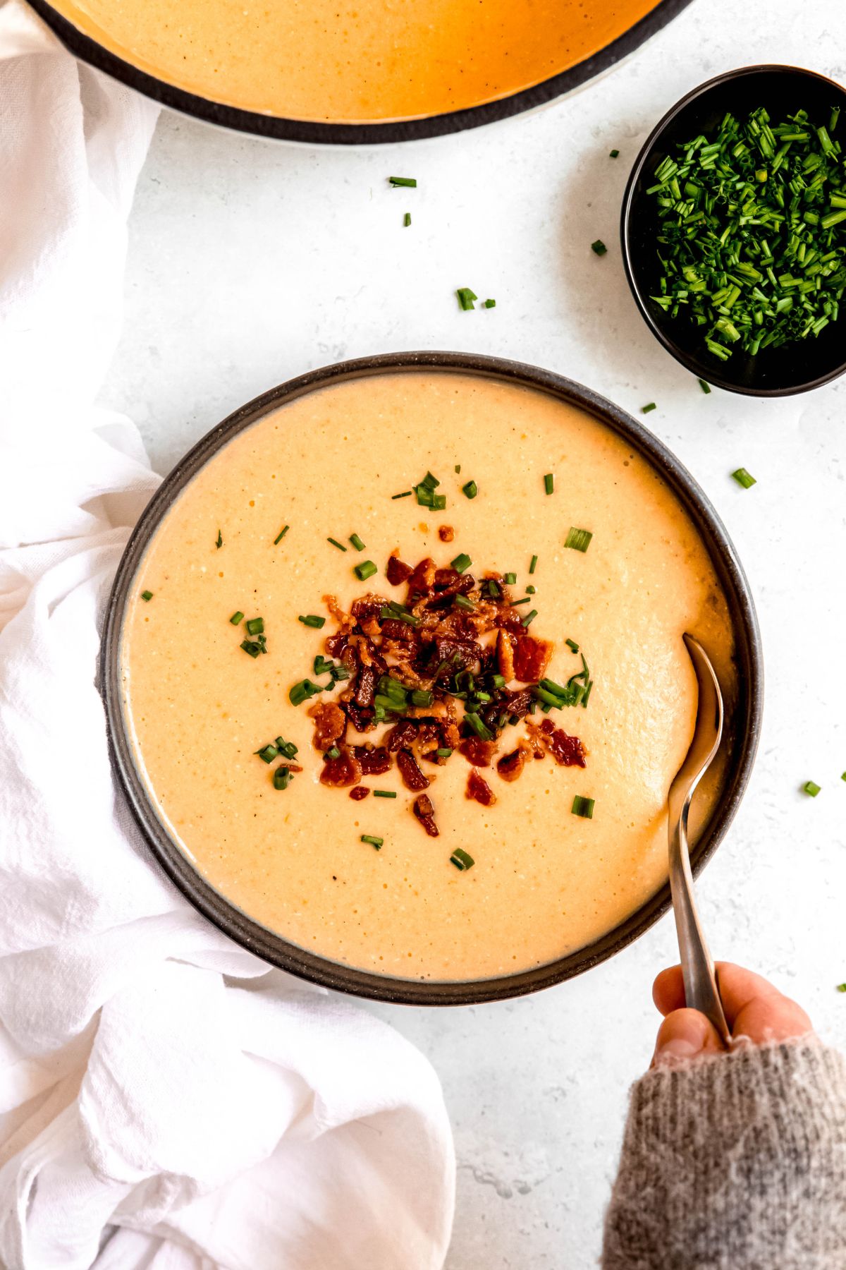 A hand scooping into a bowl of the high-protein creamy potato soup.