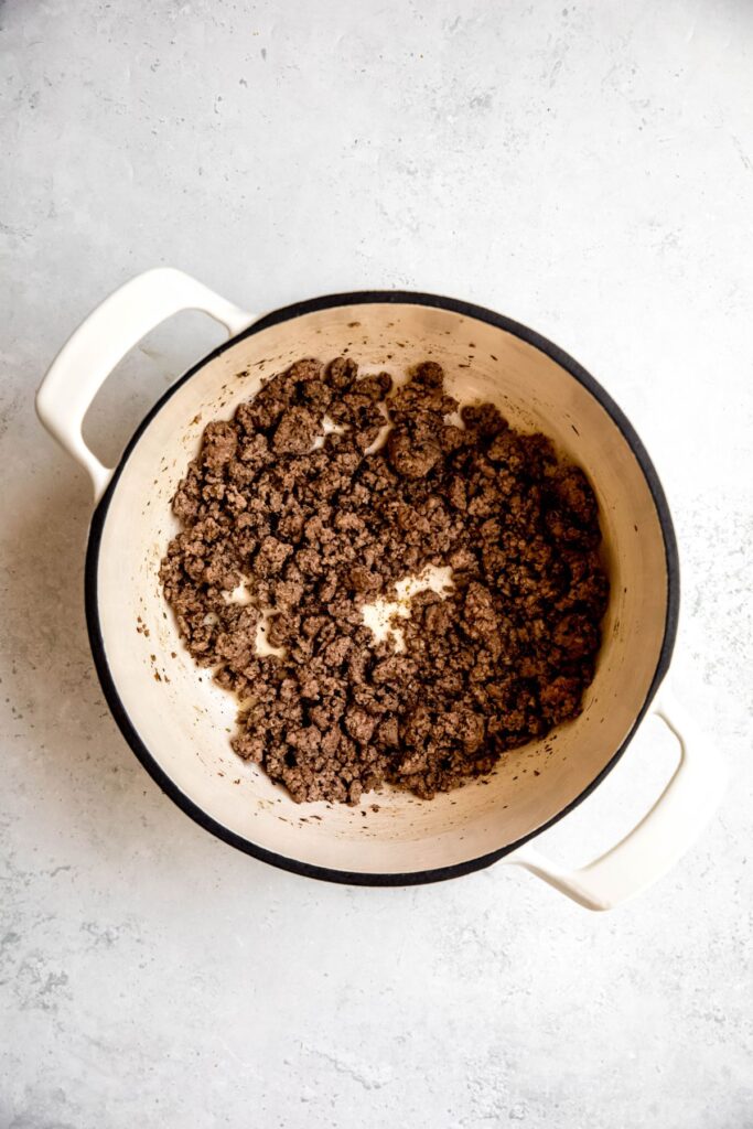 Browned ground beef in a white stock pot.