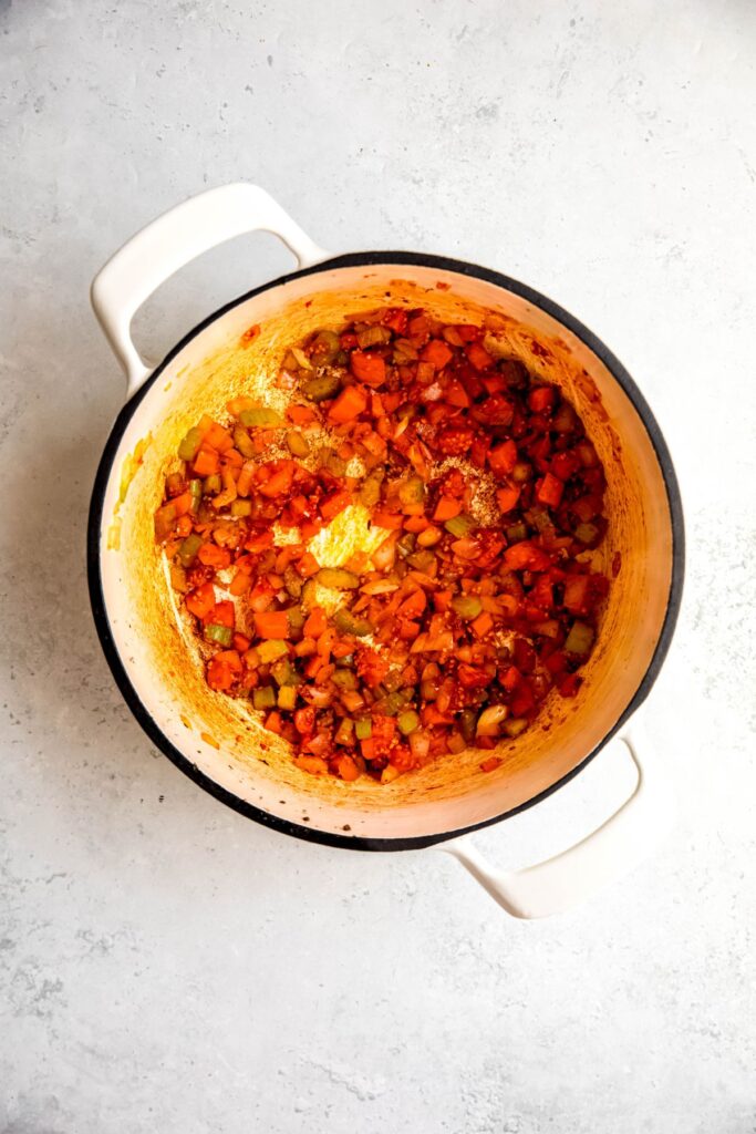 An overhead shot of sauteed mirepoix in a white Dutch oven.