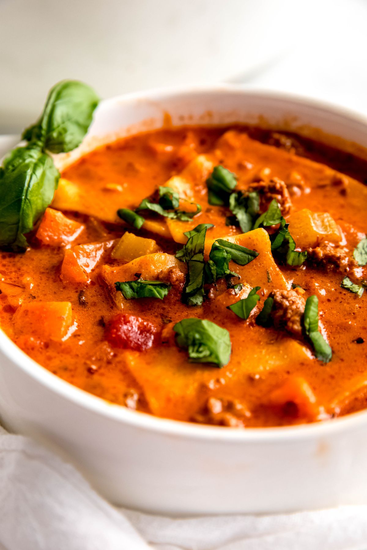A close-up shot of a bowl of lasagna soup topped with chopped basil.