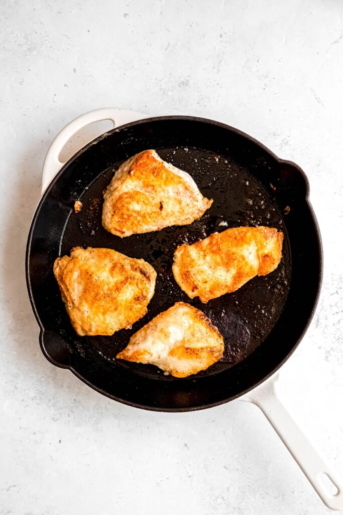 Pan-fried chicken breasts in a large white skillet.