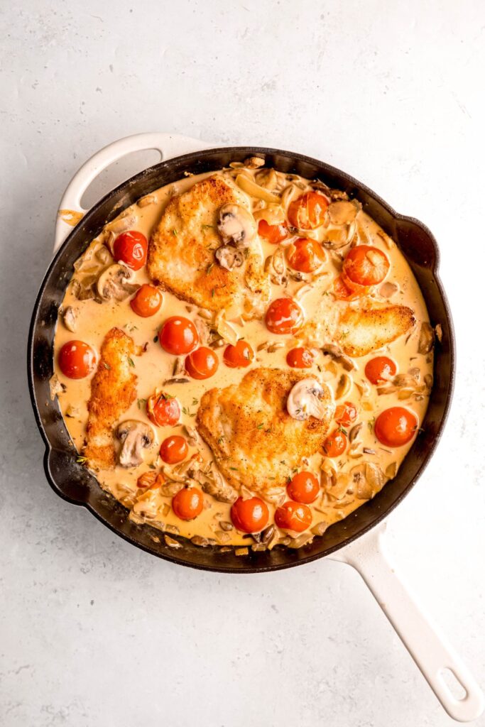 A large white skillet of creamy mushroom chicken with tomatoes.
