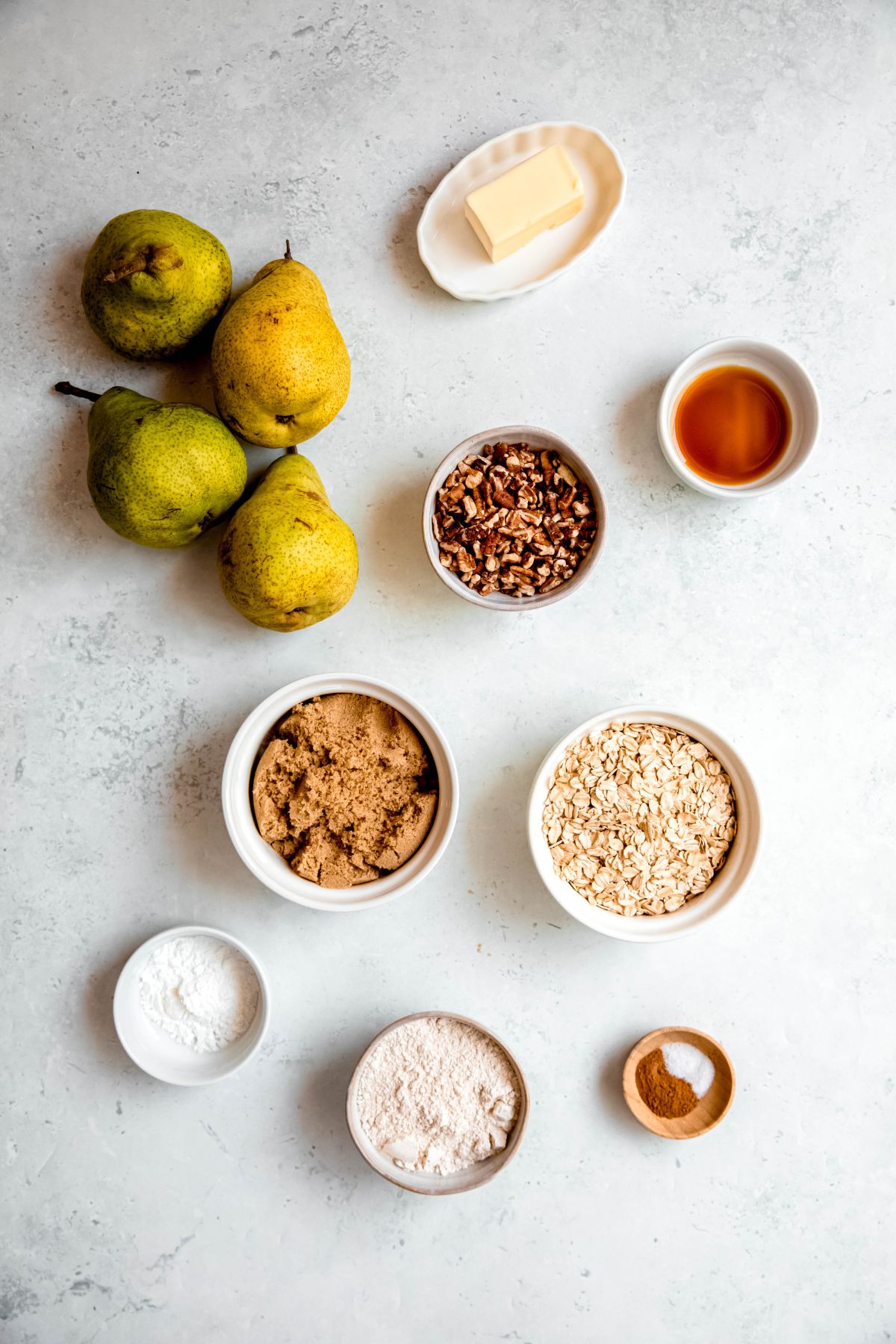 ingredients for making a pear crisp recipe with fresh pears measured out onto a white table.