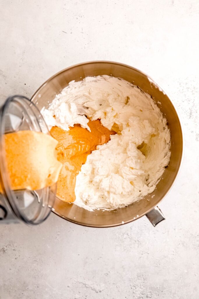 action shot of pumpkin base being poured into the bowl of whipped cream.