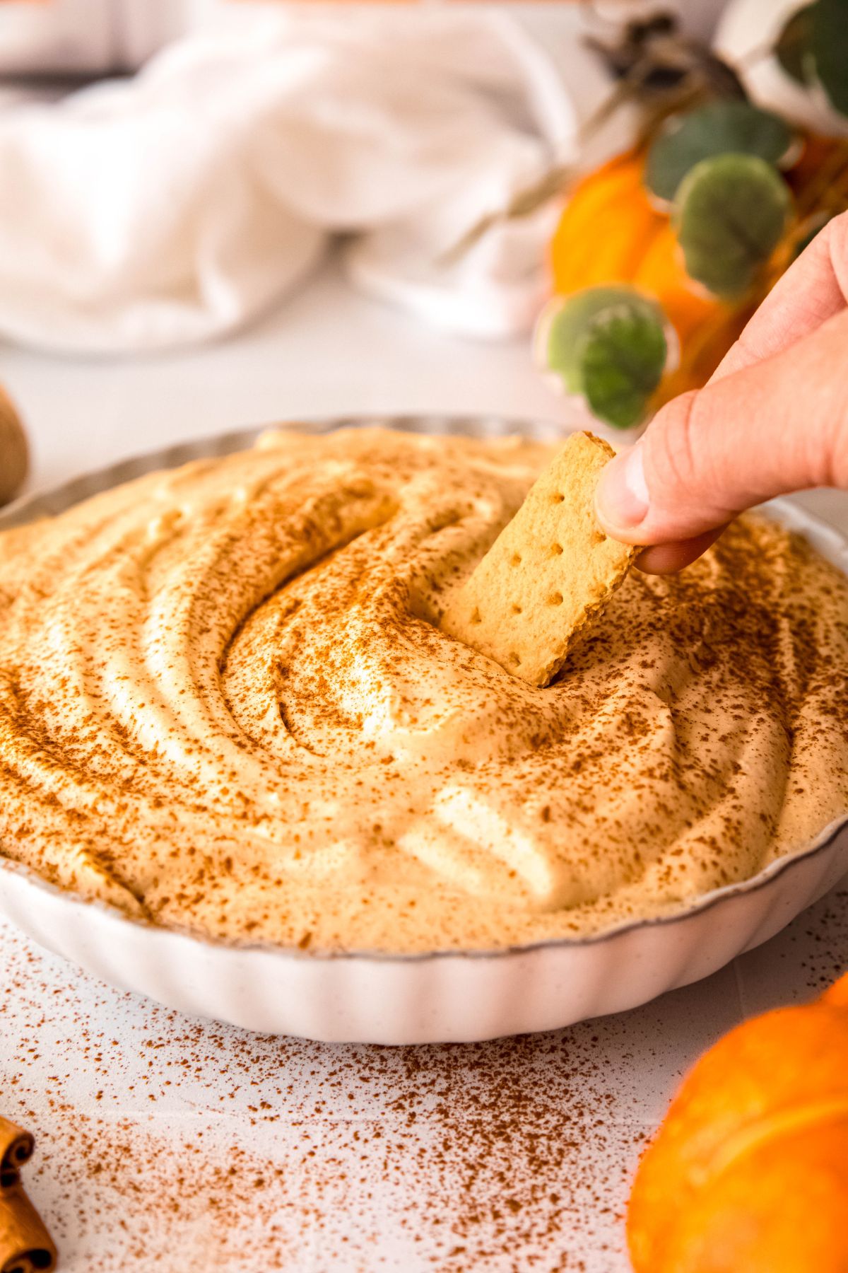 hand dipping a graham cracker into a bowl of pumpkin pie protein fluff.