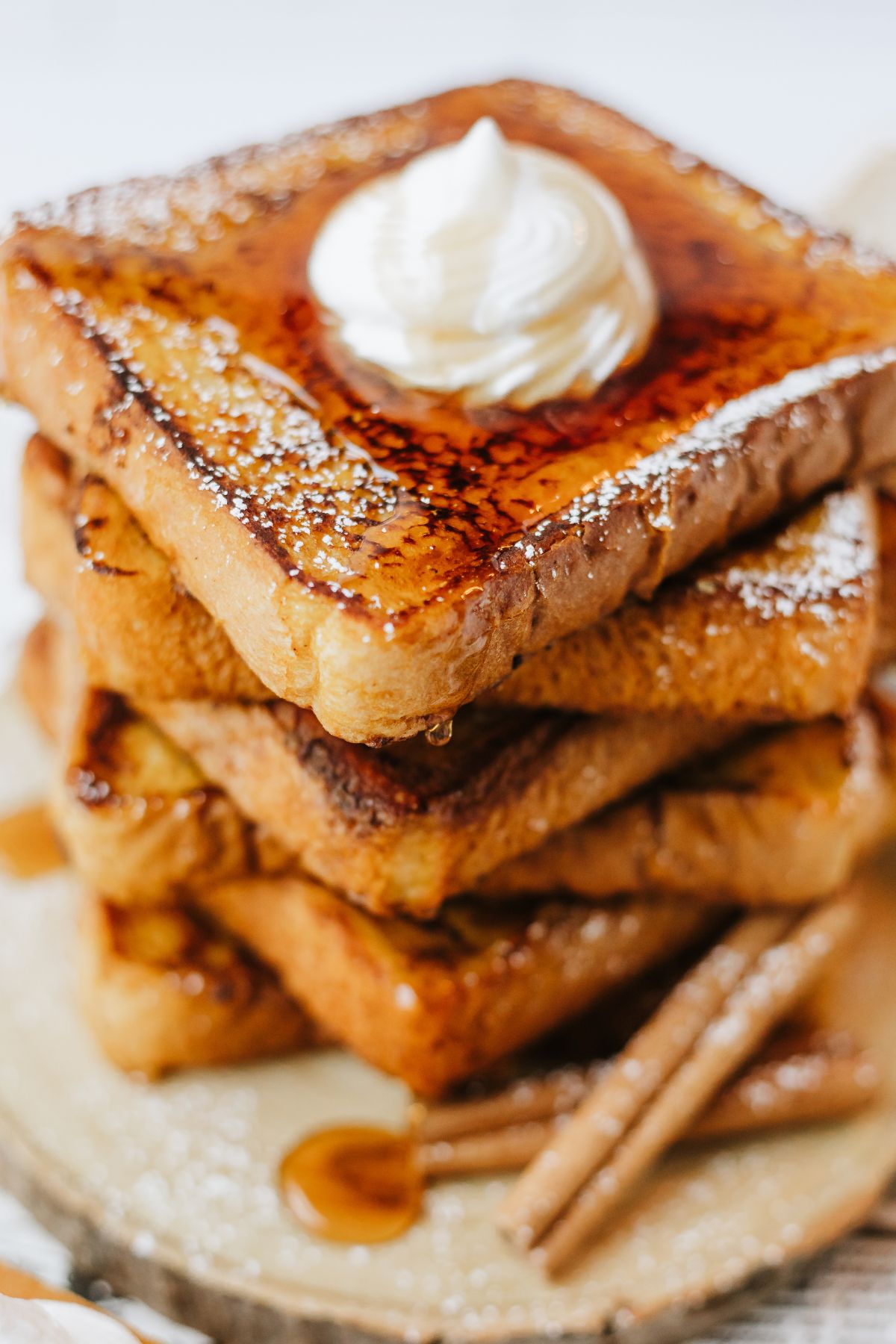 closeup shot of a stack of pumpkin spiced french toast with maple syrup dripping off the sides, a bit of powdered sugar still visible on the edges and a rosette of whipped cream on top.