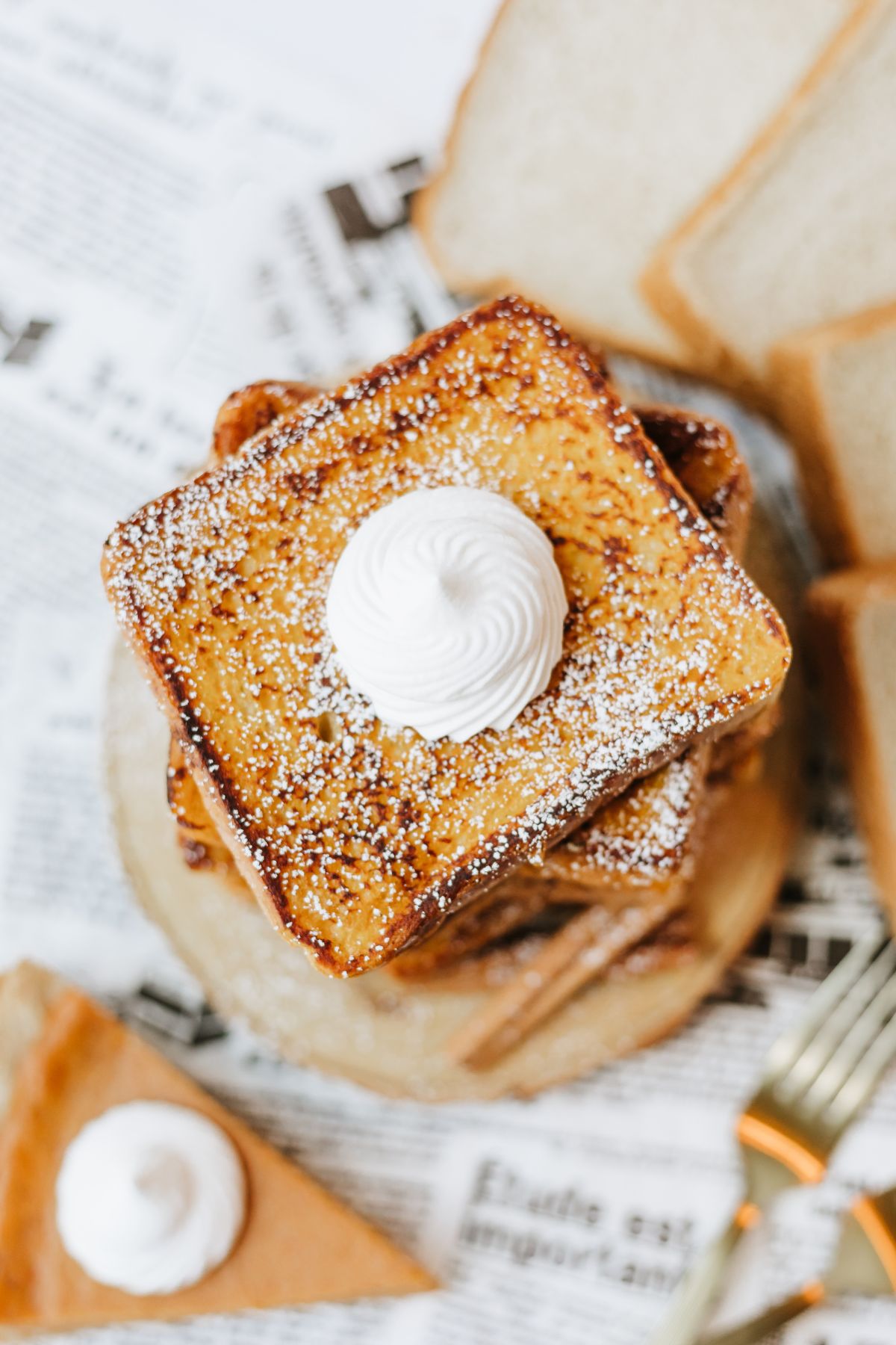 overhead shot of pumpkin french toast in a stack with each slice rotated 45 degrees from the one underneath it to create a star pattern; the stack is topped with whipped cream and powdered sugar.