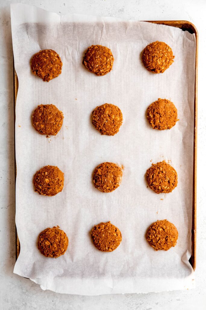 12 raw oatmeal and pumpkin cookies on a parchment lined baking sheet.