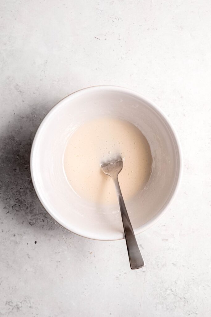 milk and powdered sugar glaze in a small white bowl after mixing with a fork.