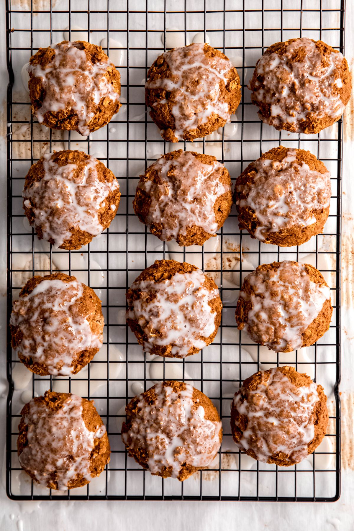 pumpkin oatmeal cookies on a wire rack and drizzled with glaze; there's a lined sheet pan underneath to catch the glaze that drips off.