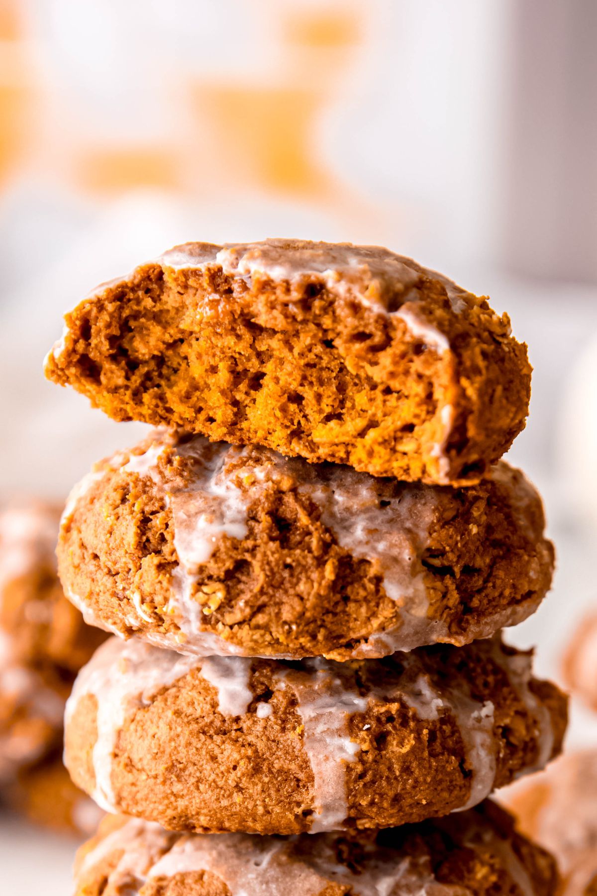 side on shot of a stack of thick and chewy glazed oatmeal pumpkin cookies with the top one broken in half to show the thick, moist texture.