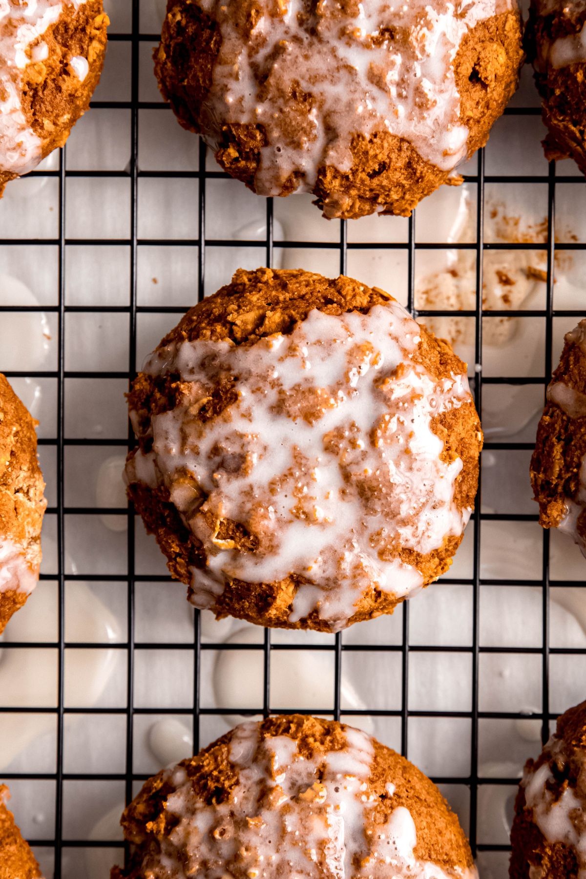 closeup shot of the creamy white glaze added to the top of healthy pumpkin oatmeal cookies on a wire rack.