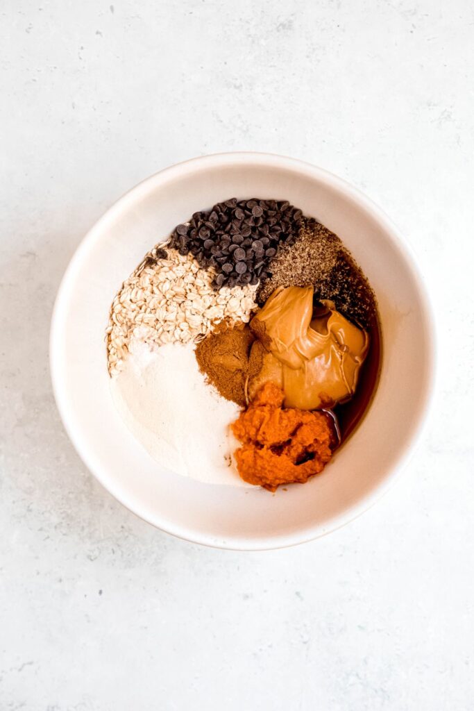 all the ingredients for pumpkin protein balls added to a large white mixing bowl.