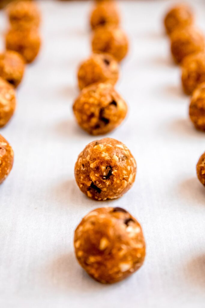 shaped pumpkin protein energy bites on a parchment-lined sheet tray for chilling.