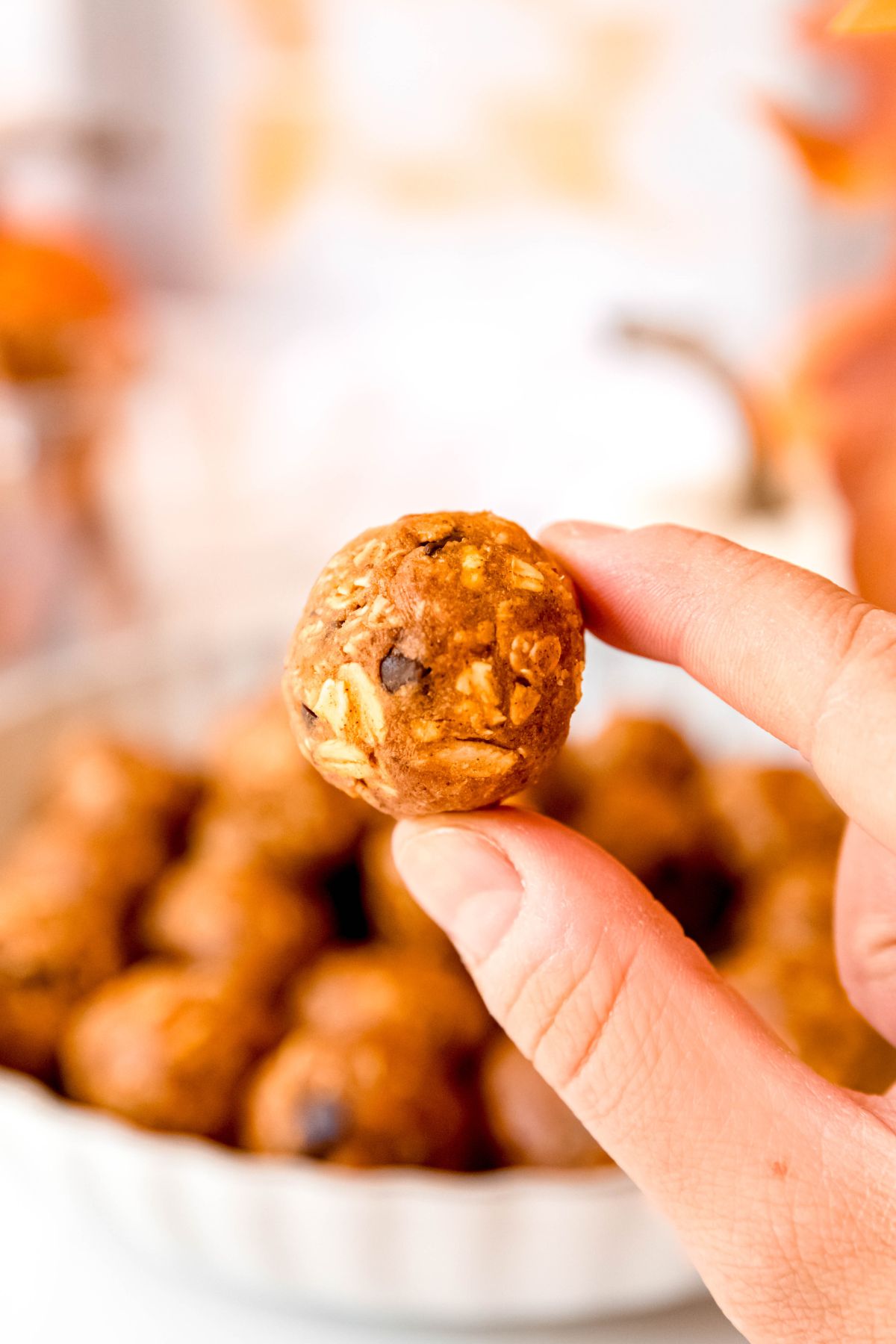 single chocolate chip pumpkin protein ball being held by a forefinger and thumb in front of the rest of the bowl that's blurred out in the background.