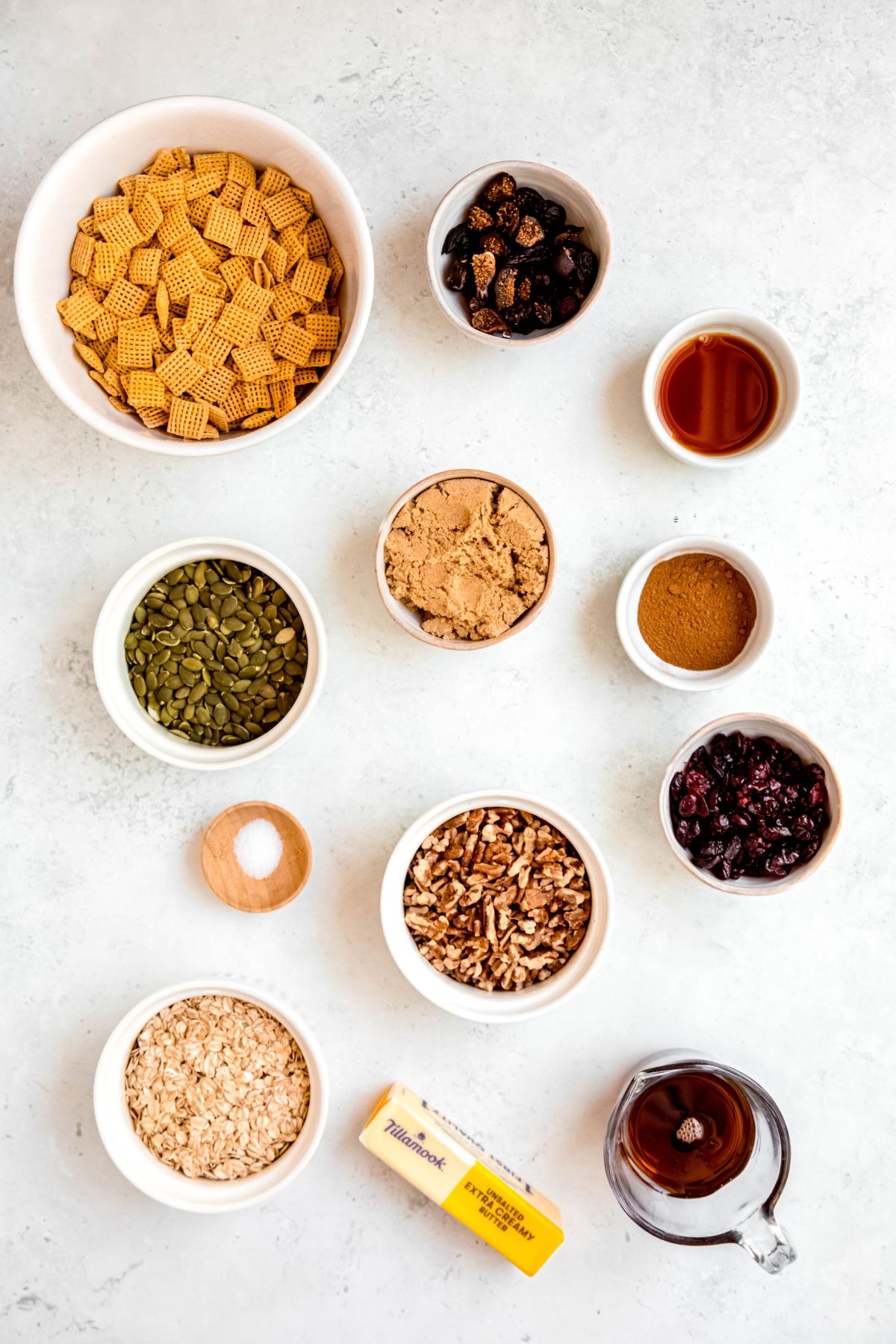 ingredients for making pumpkin spice chex mix recipe measured out in white bowls on a white table.
