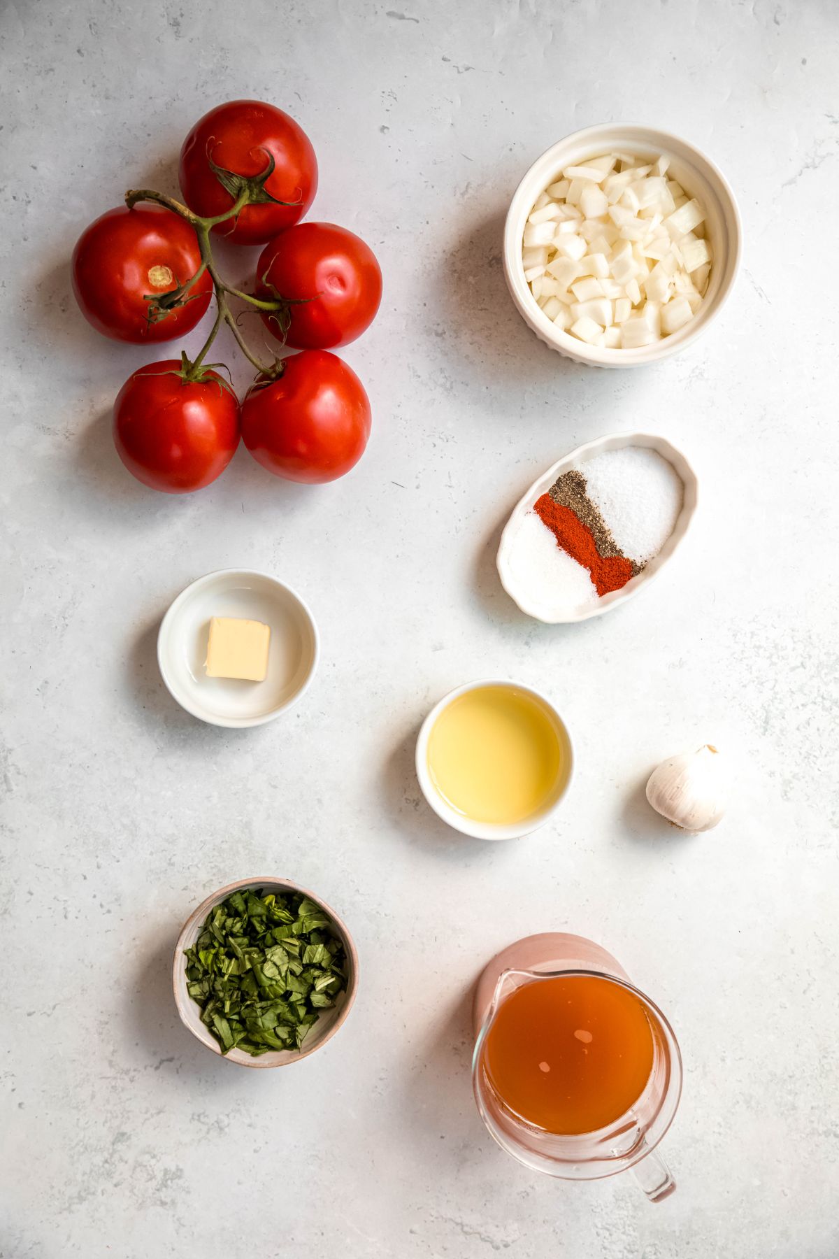 ingredients to make roasted tomato soup recipe with fresh tomatoes and basil measured out on a white table.