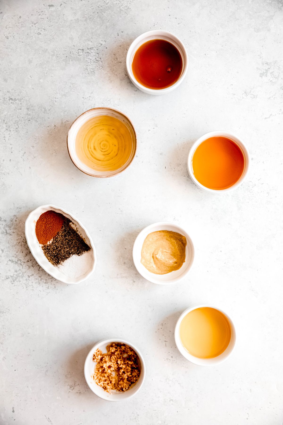 ingredients for apple cider vinaigrette recipe measured out into white bowls on a white table.