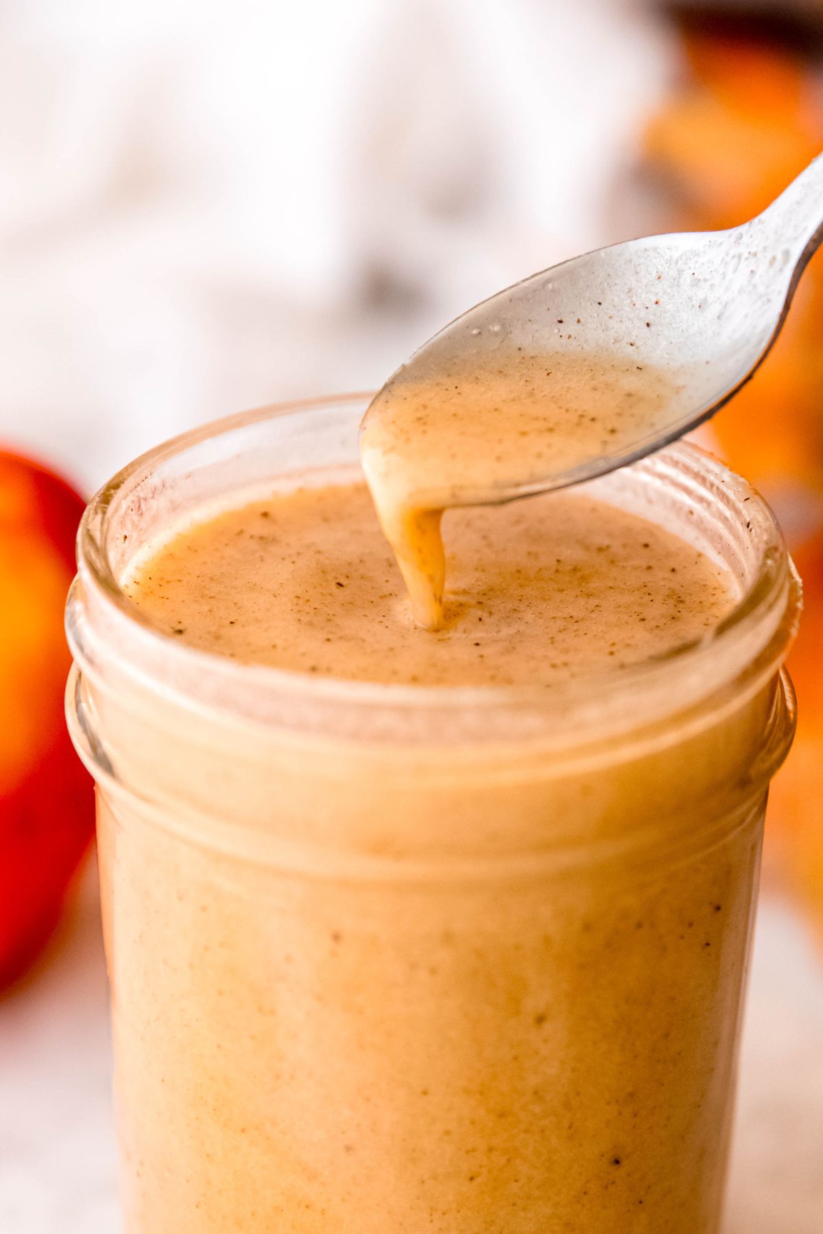 silver spoon drizzling some homemade creamy apple cider vinaigrette into a mason jar filled with it; you can see the viscous consistency.