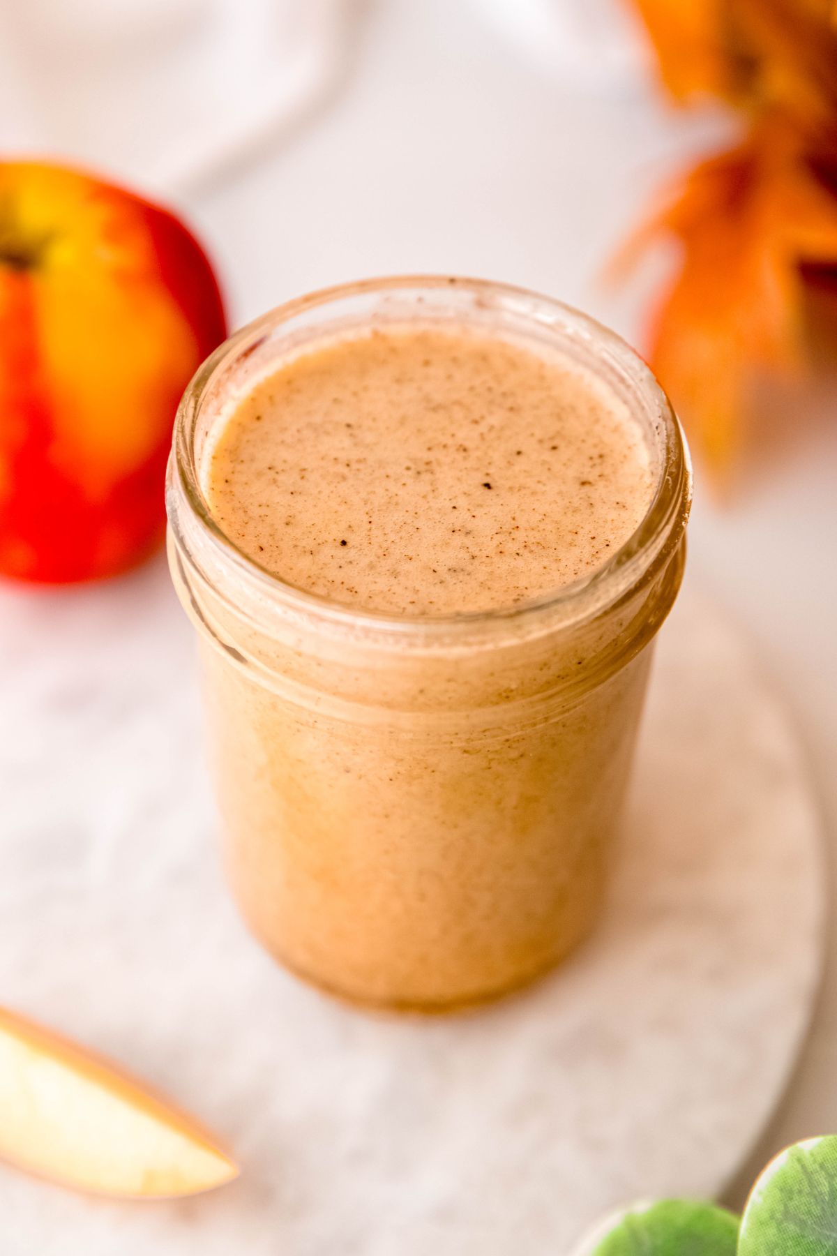 45 degree angle downward shot into a small mason jar filled with homemade apple cider vinaigrette dressing flecked with black pepper and cinnamon.
